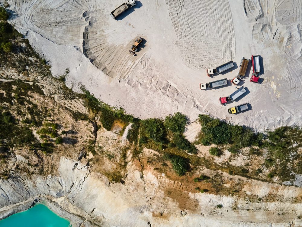 Aerial view trucks near quarry extraction porcelain clay, kaolin, with turquoise water and white shore, drone view open pit mine kaolin flooded with water